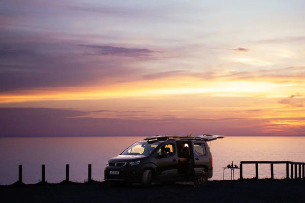 Hochdachkombi am Meer bei Sonnenuntergang mit Campingtisch neben dem Fahrzeug
