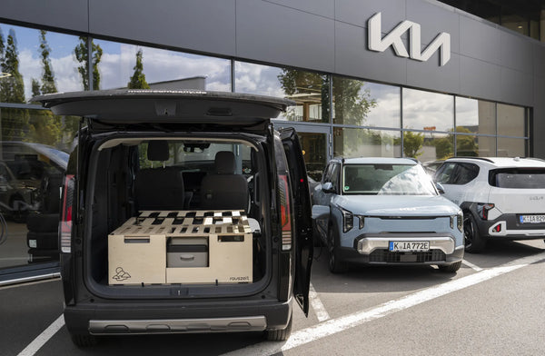 Campingbox im Kia PV5 Passenger mit offener Heckklappe vor einem Kia-Autohaus