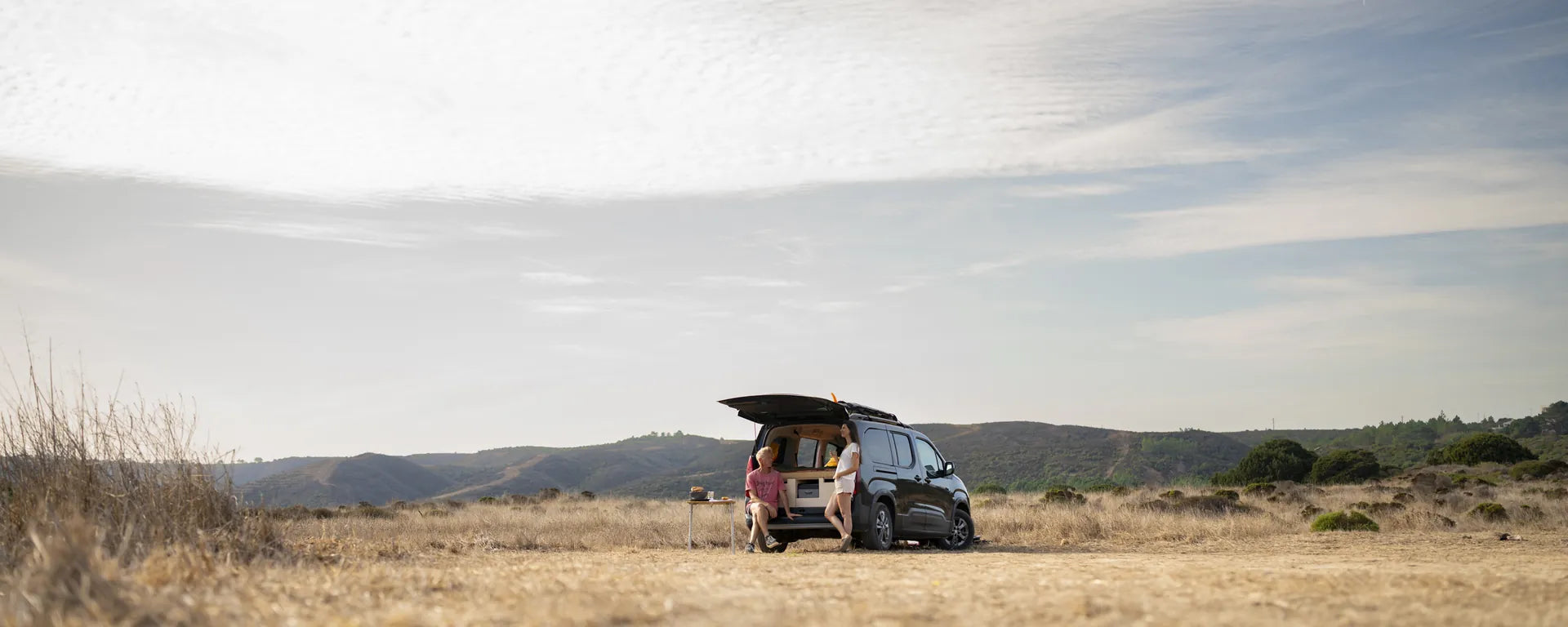 Hochdachkombi mit Campingbox in weiter Algarve-Landschaft mit Paar am offenen Heck
