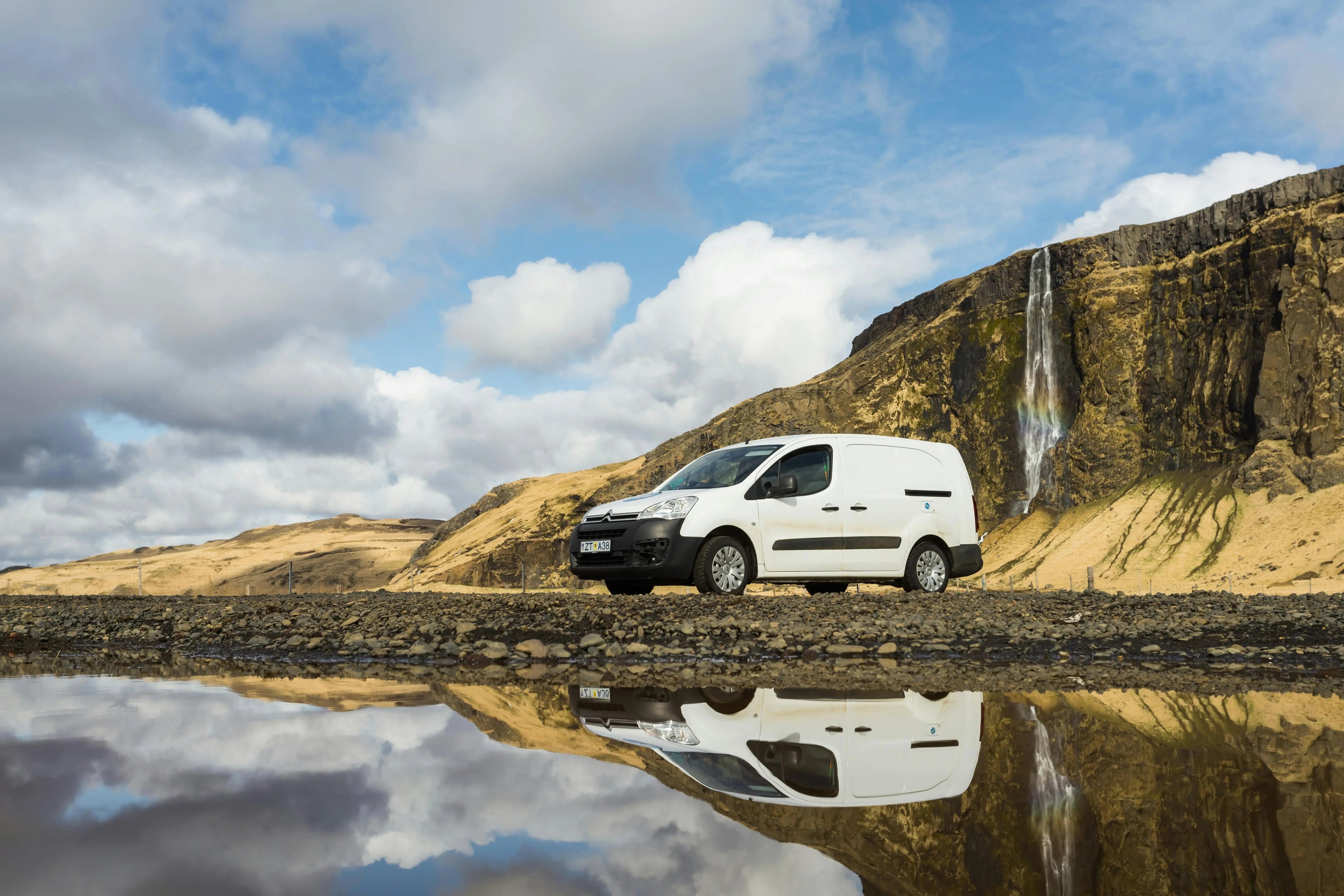 Weißer VW Caddy vor Wasserfall und Berglandschaft mit Spiegelung im Wasser