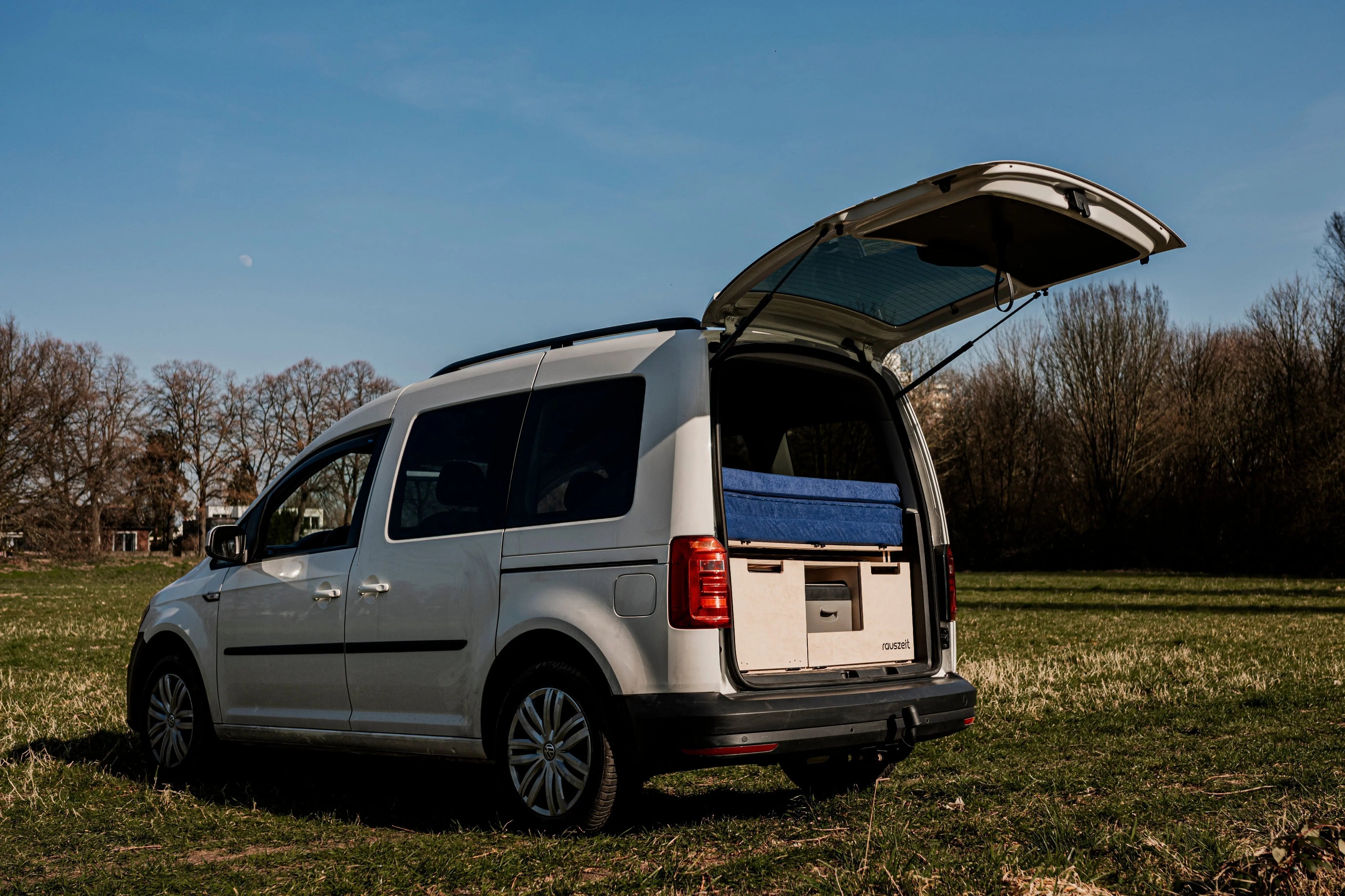 Rauszeit Campingbox eingebaut im VW Caddy mit geöffneter Heckklappe auf Wiese