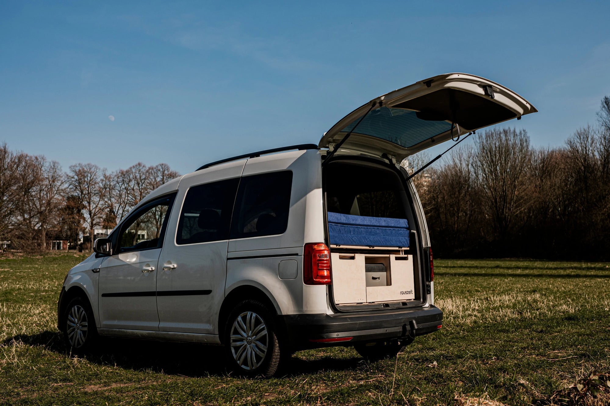 Campingbox eingebaut im VW Caddy mit geöffneter Heckklappe auf einer Wiese
