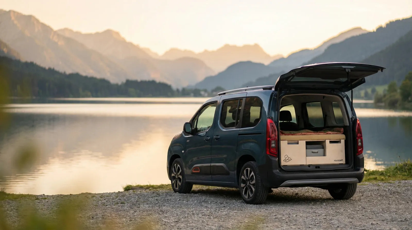 Citroën Berlingo mit Campingbox am See bei Sonnenuntergang mit Bergspiegelung im Wasser