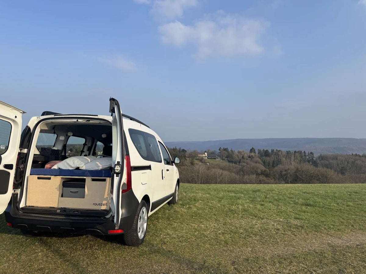 Weißer Dacia Dokker mit offenen Hecktüren und eingebauter Rauszeit Campingbox auf einer Wiese in der Eifel