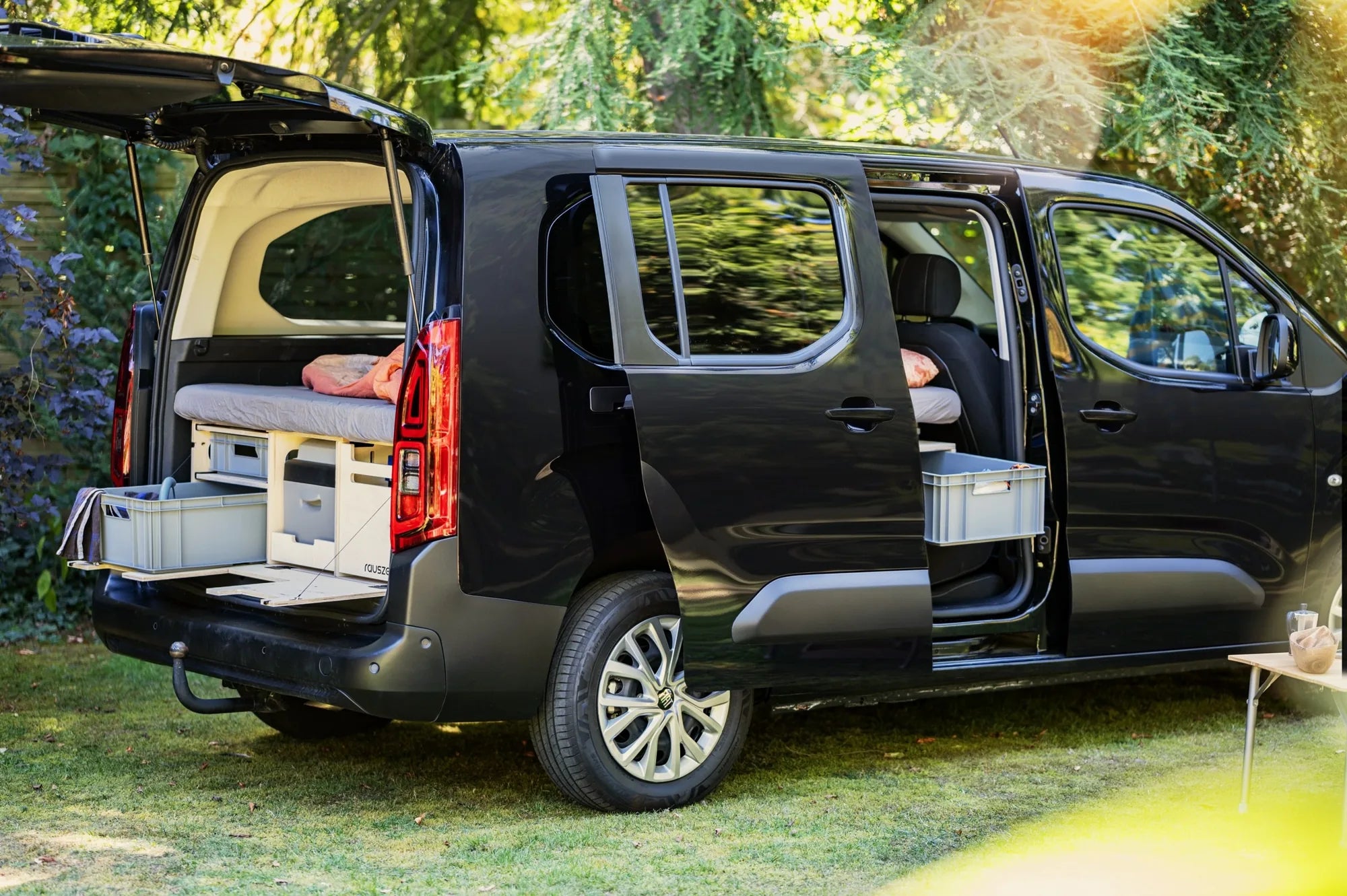 Fiat Doblò mit Rauszeit Campingbox im Heck, Heckklappe und Schiebetür offen, im Garten