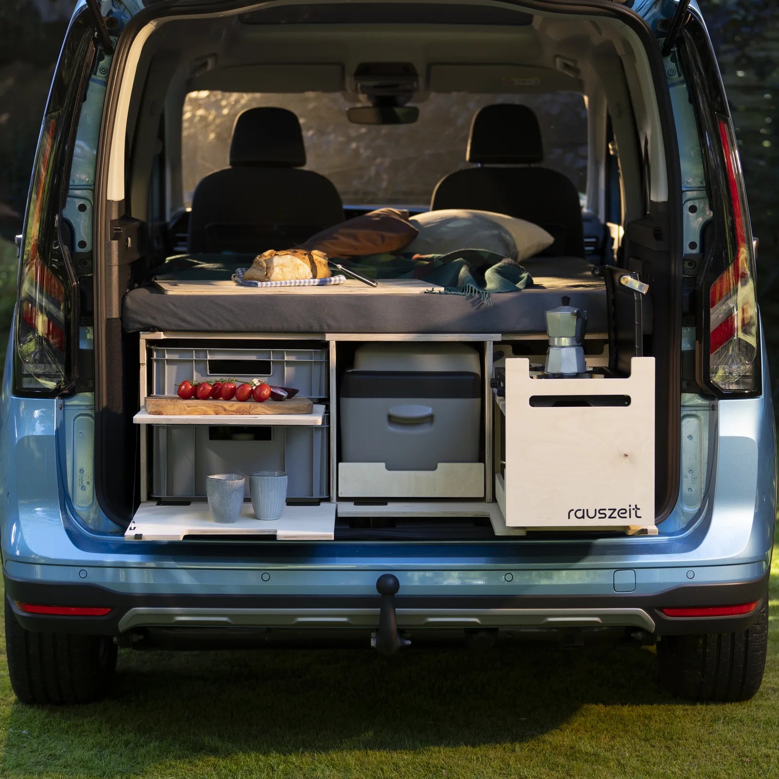 Rauszeit Campingbox im Heck eines hellblauen Ford Tourneo Connect, frontal von hinten: Schiebebett, Euroboxen, Kühlbox und Kochmodul