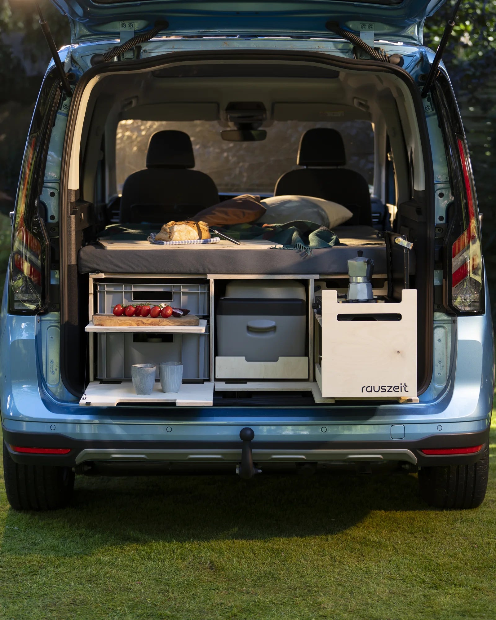 Rauszeit Campingbox im Heck eines hellblauen Ford Tourneo Connect, frontal von hinten: Schiebebett, Euroboxen, Kühlbox und Kochmodul