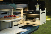 Heckküche der Campingbox von der Seite: Kochmodul mit Gaskocher und Espressokanne, Schneidebrett, Euroboxen und Bett