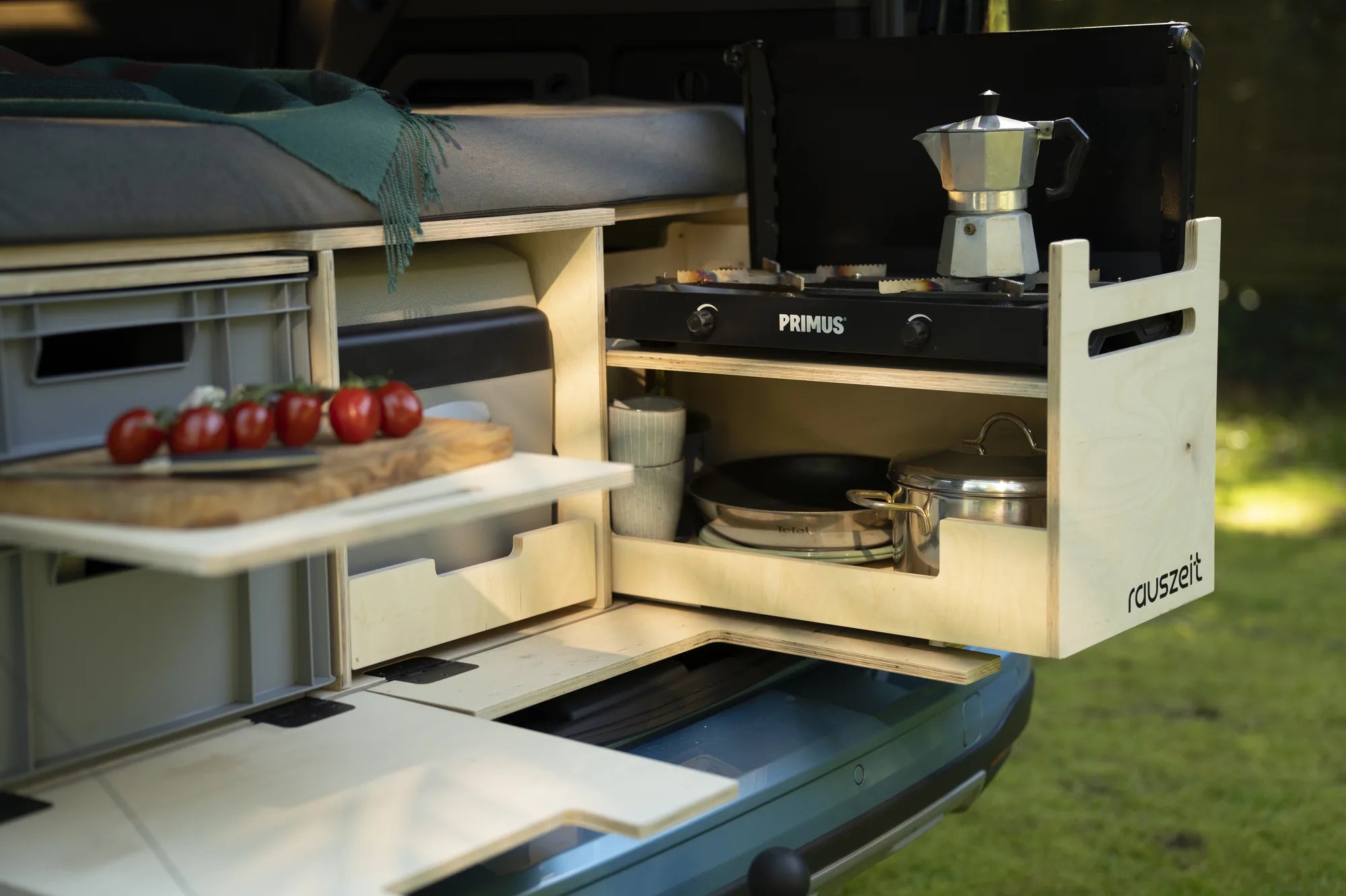 Heckküche der Campingbox von der Seite: Kochmodul mit Gaskocher und Espressokanne, Schneidebrett, Euroboxen und Bett