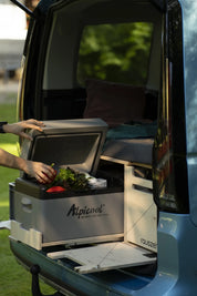 Kühlbox auf dem ausgezogenen Auszug der Campingbox am offenen Heck, eine Hand nimmt Gemüse heraus