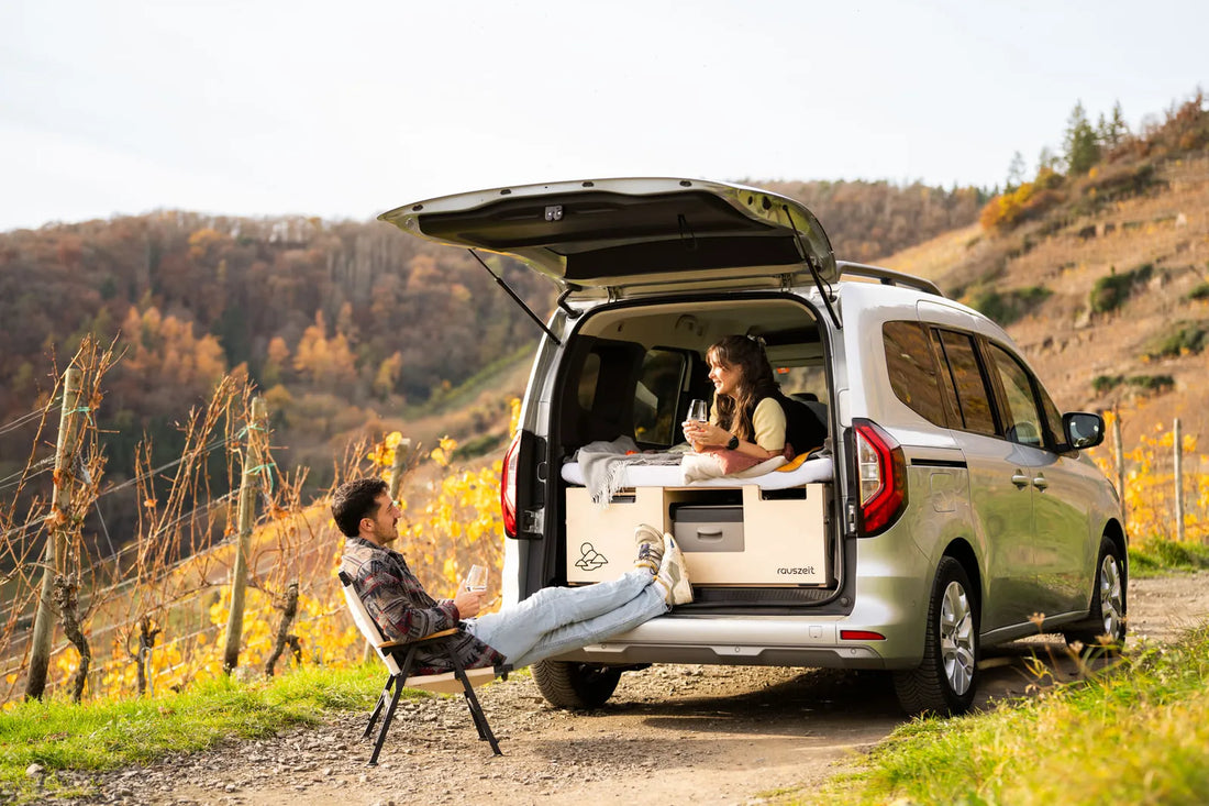 Paar entspannt an der offenen Campingbox vor Weinbergen im Herbst