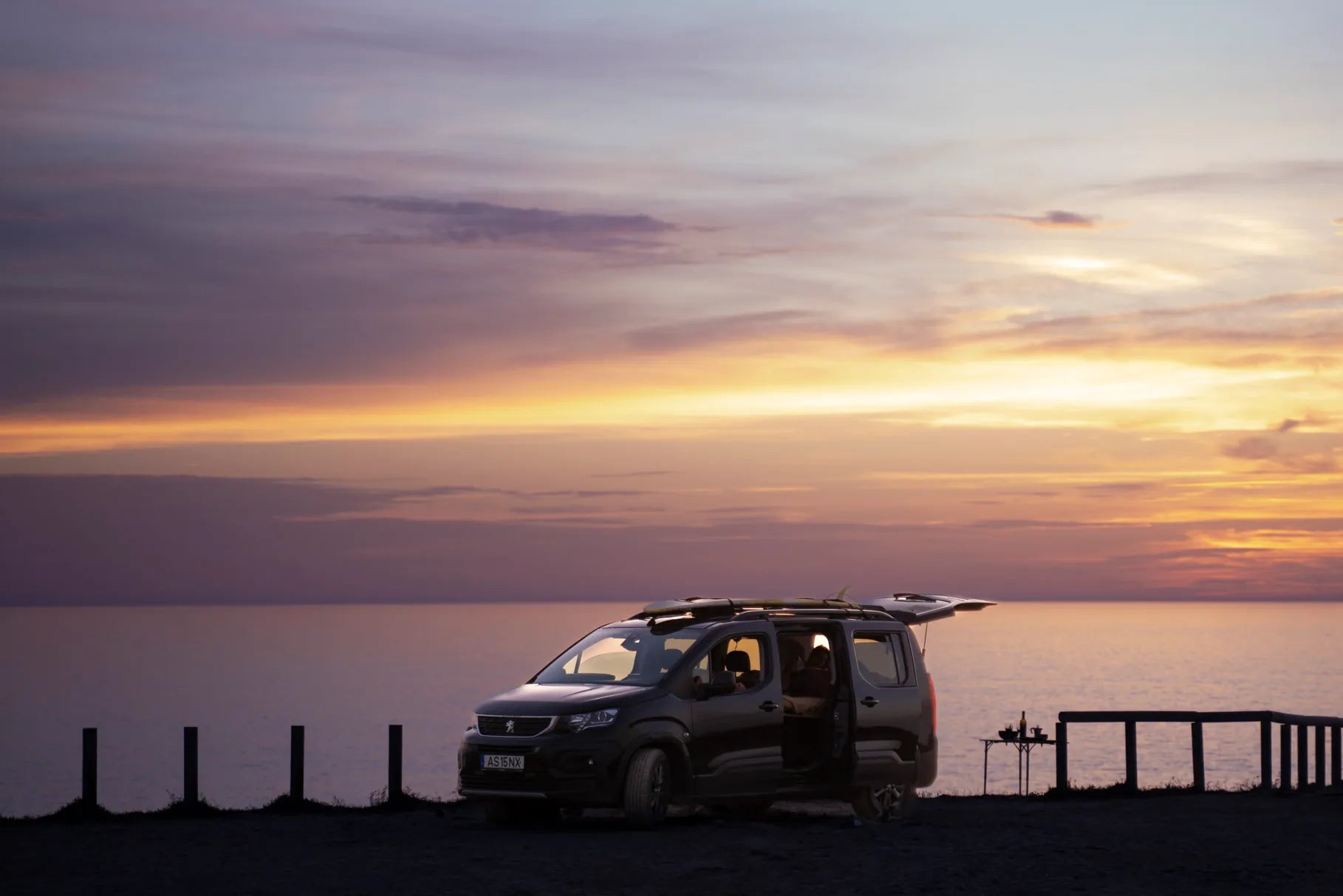 Peugeot Rifter mit Surfbrett auf dem Dach an der Küste Portugals bei Sonnenuntergang