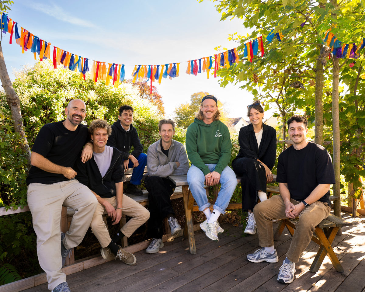 Team aus sieben Leuten sitzt lachend auf Holzbänken unter bunten Wimpelketten